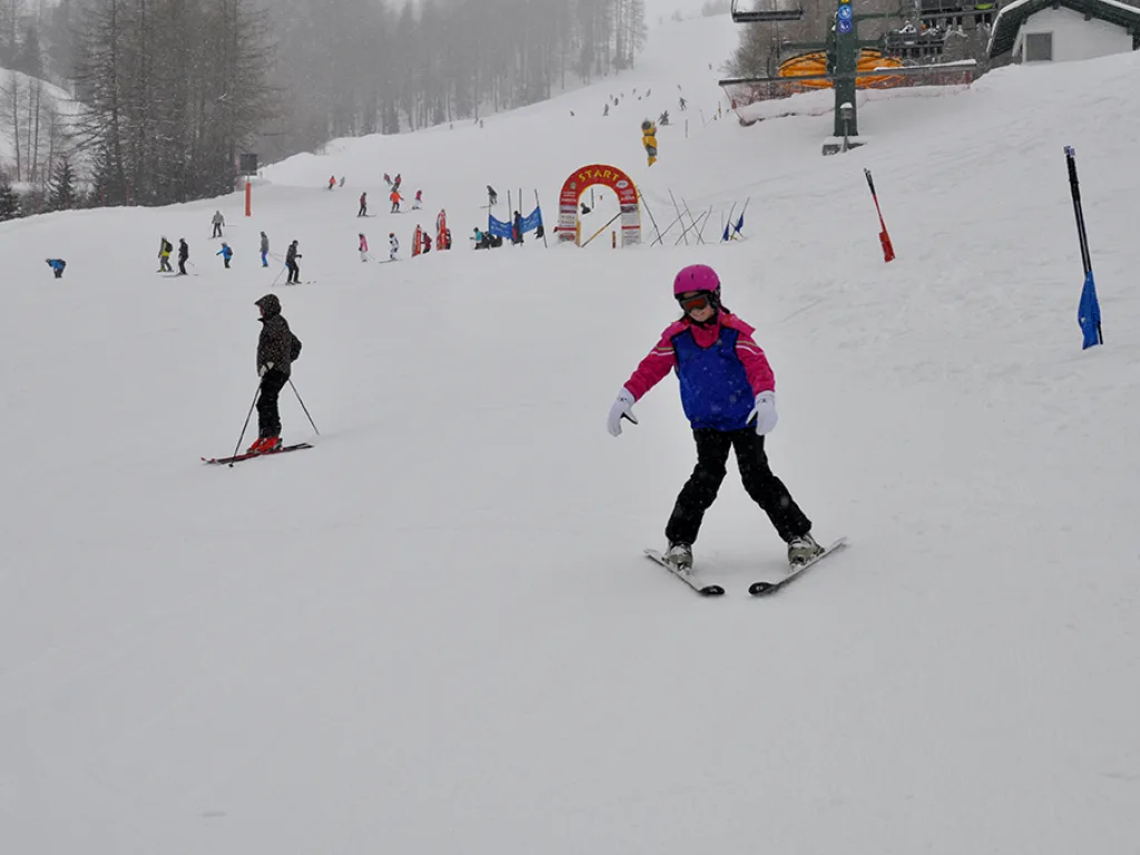 Skifahrerin in pinker Jacke auf der Piste vor der Talstation.